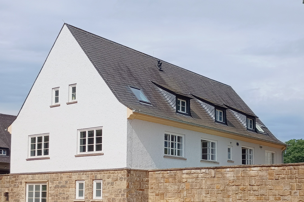 Ein weiß verputztes Gebäude mit Satteldach vor einem blauen Himmel