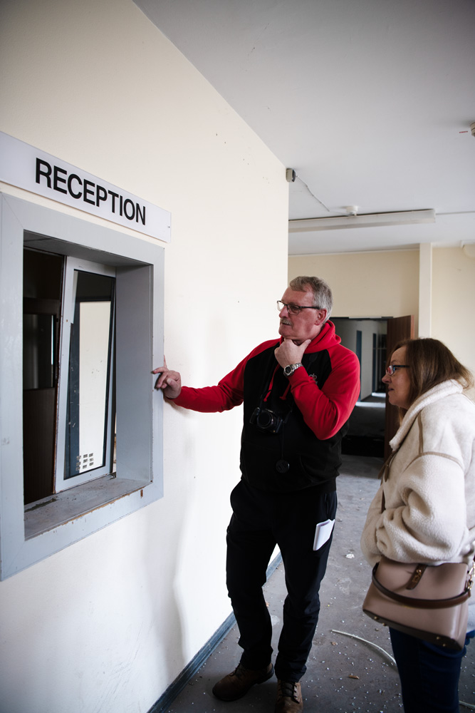 Ein Mann und eine Frau stehen neben einem Fenster in einer Wand, über dem „Reception“ steht