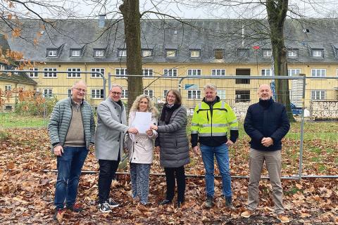 Personengruppe vor einem Gebäude präsentiert einen Vertrag