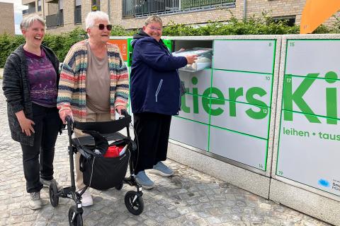 Drei Frauen neben einer Ausleihstation mit der Aufschrift „Quartierskiste“