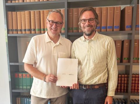 Zwei Männer vor Bücherregal mit einem Dokument